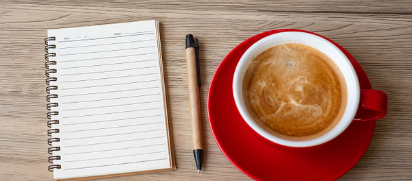 Notebook and pen on a table with a warm drink and soft light